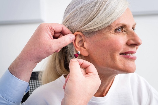 Ältere Frau bekommt ein Hörgerät angepasst, Hörakustiker berät zur Hörgeräteversorgung.